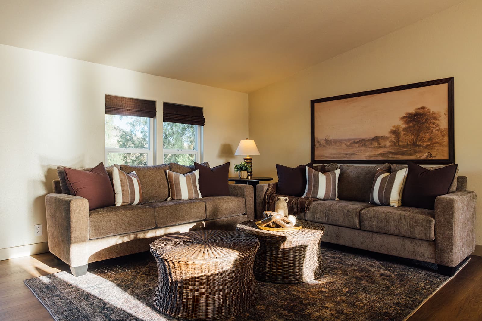 Living room with two sofas, woven coffee tables, and a framed landscape