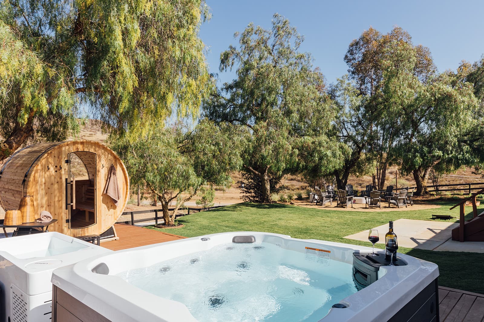 Outdoor wellness deck at golden hour — hot tub, cold plunge, and barrel sauna